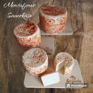 Montafoner Sauerkäse in verschiedenen Größen serviert auf drei Holzbrettern. Der vordere Sauerkäse ist angeschnitten. Der Hintergrund ist aus Holz