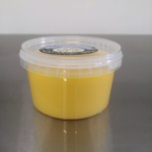 Montafoner Butterschmalz, verpackt in einer Plastikdose, steht von der Seite fotografiert auf einem Edelstahltisch.