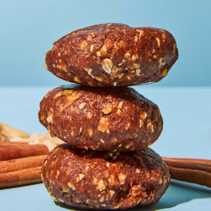 Drei dunkelbraune Bio Energy Balls liegen ausgepackt aufeinander vor einem blauen Hintergrund