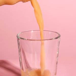 Ingwershot wird in ein Glas gegossen vor rosa Hintergrund