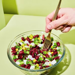 Eine durchsichtige Schüssel ist angerichtet mit Salat und Kidneybohnen. Mit Stäbchen wird daraus gegessen. Der Hintergrund ist grün.