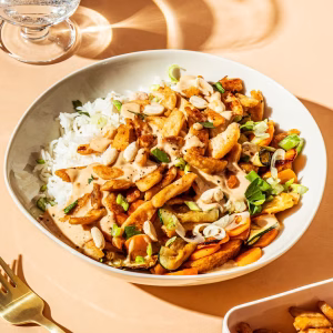 Ein weißer Teller ist angerichtet mit gekochten Sojastreifen, Reis und Gemüse. Daneben liegt eine Gabel vor rosa Hintergrund