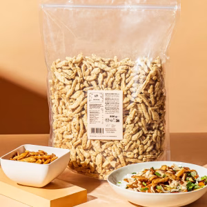 Sojastreifen stehen in einer Plastikverpackung, davor eine Schüssel mit Essen angerichtet, vor orang-farbenem Hintergrund