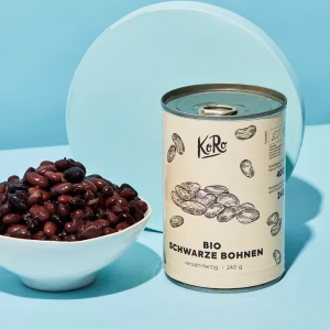 Eine Dose schwarze Bio Bohnen und eine weiße Schüssel mit offenen schwarzen Bohnen stehen vor blauem Hintergrund